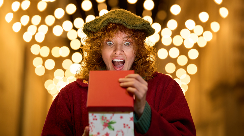 Excited woman opening christmas gift under string lights